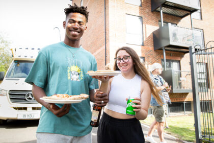 two people smile holding pizza and drinks